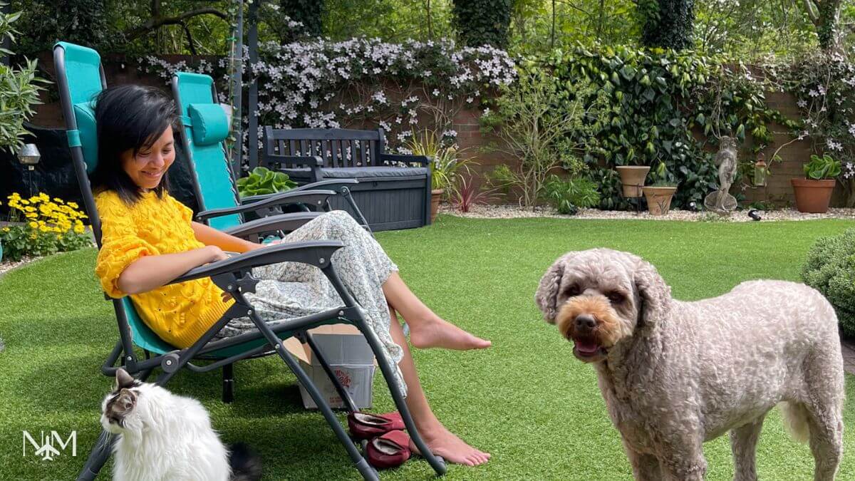 Beatrice sitting on a chair in the garden while pet sitting a Norwegian Forest cat and a labradoodle. They all look happy