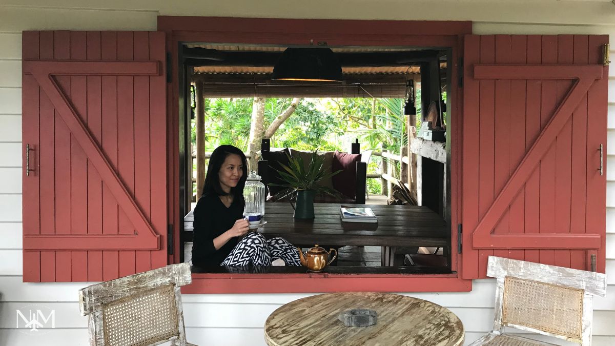 Beatrice woman sitting with a cup of tea by the large open windows in the main Reception area of La Vieille Cheminée guesthouse 