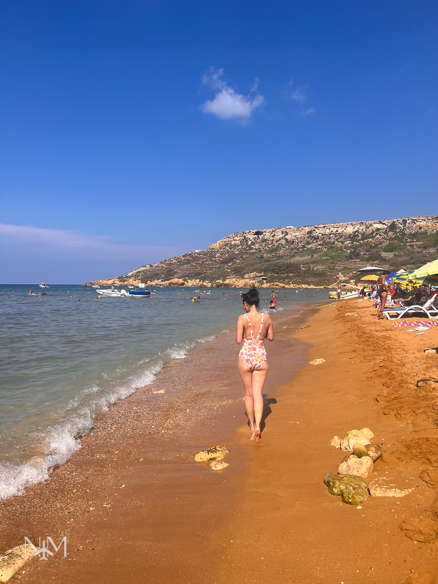 Beatrice of the Nomadic Mauritians in her swimsuit walking down the beach at Ramla Bay, Gozo